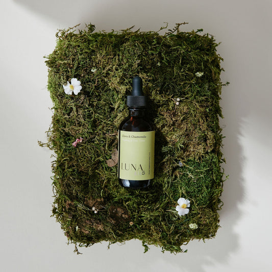 Photograph of Subluna Clove & Chamomile baby drops bottle on moss with flowers, featured at Born Primal in Australia